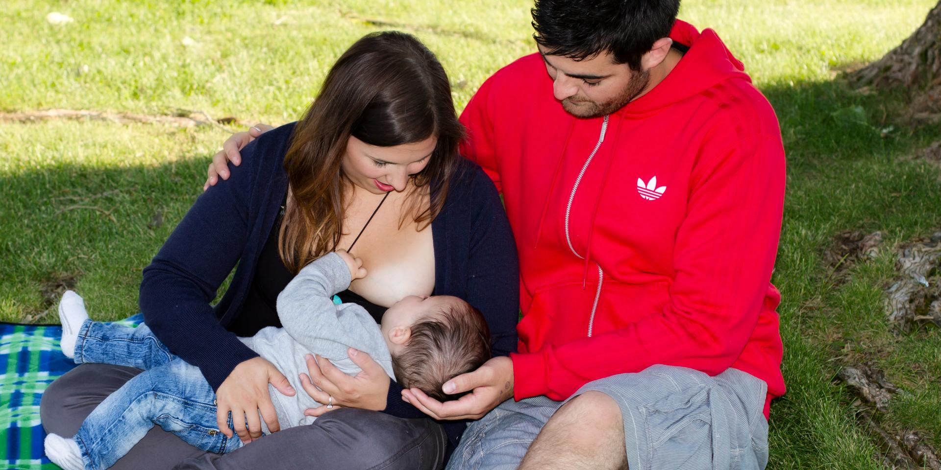 Man sits next to his wife who is breastfeeding their baby Man sits next to his wife who is breastfeeding their baby
