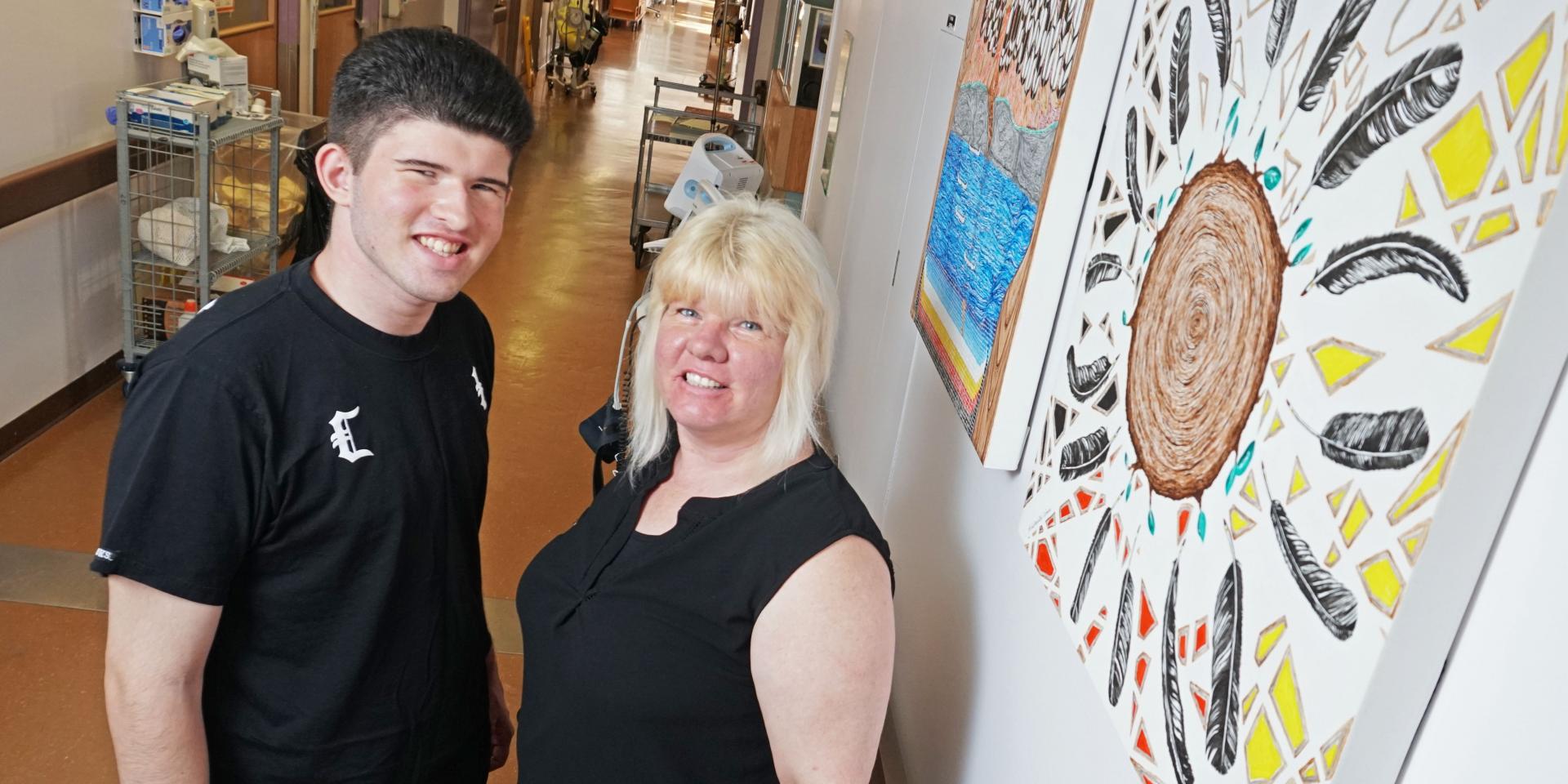 Darene Gallie and son Joey Raposo standing in front of Healing Room paintings