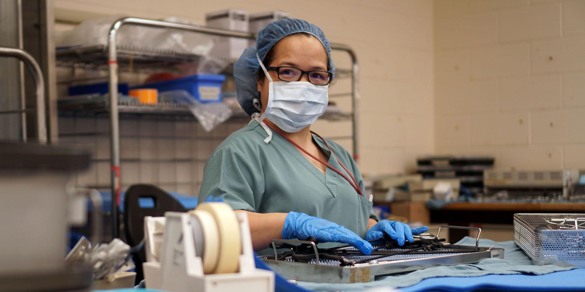 Adela wearing PPE touching a tray of instruments