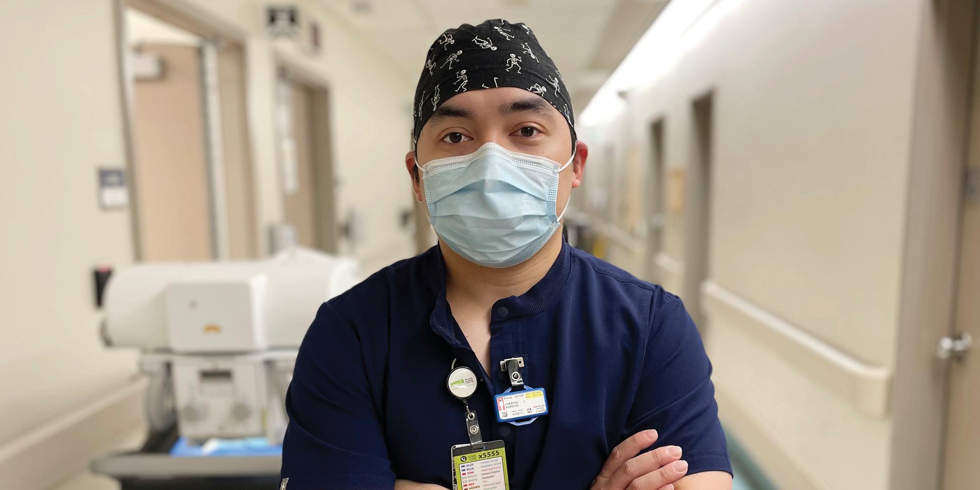 A hospital worker stands in a hallway looking at the camera