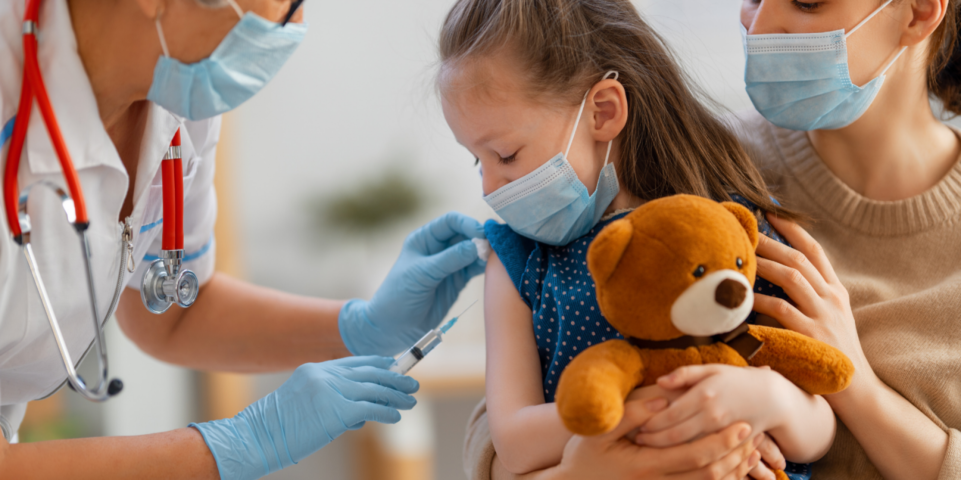 A child holds a stuffed bear while they are being vaccinated by a nurse.