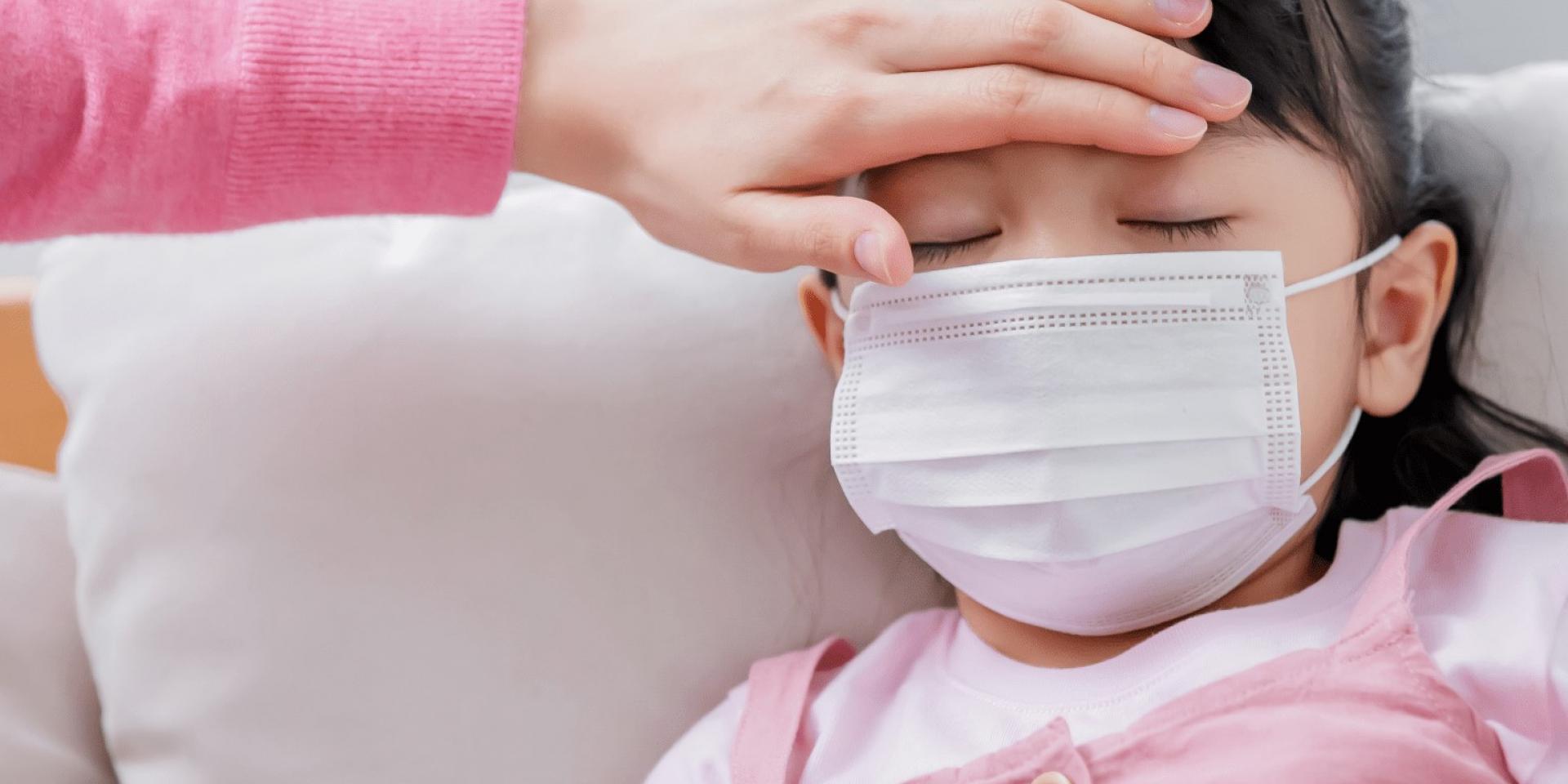 Hand on a childs forehead checking their temperature.