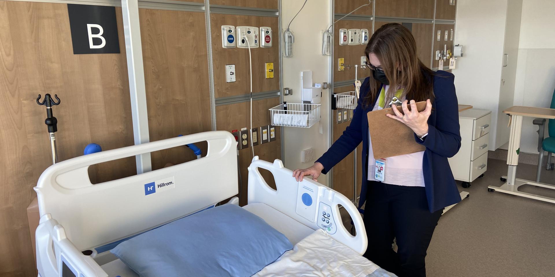 Carolyn Hay, Project Manager of the Redevelopment team at Michael Garron Hospital, stands on the left side of an inpatient bed in the new Thomson Centre