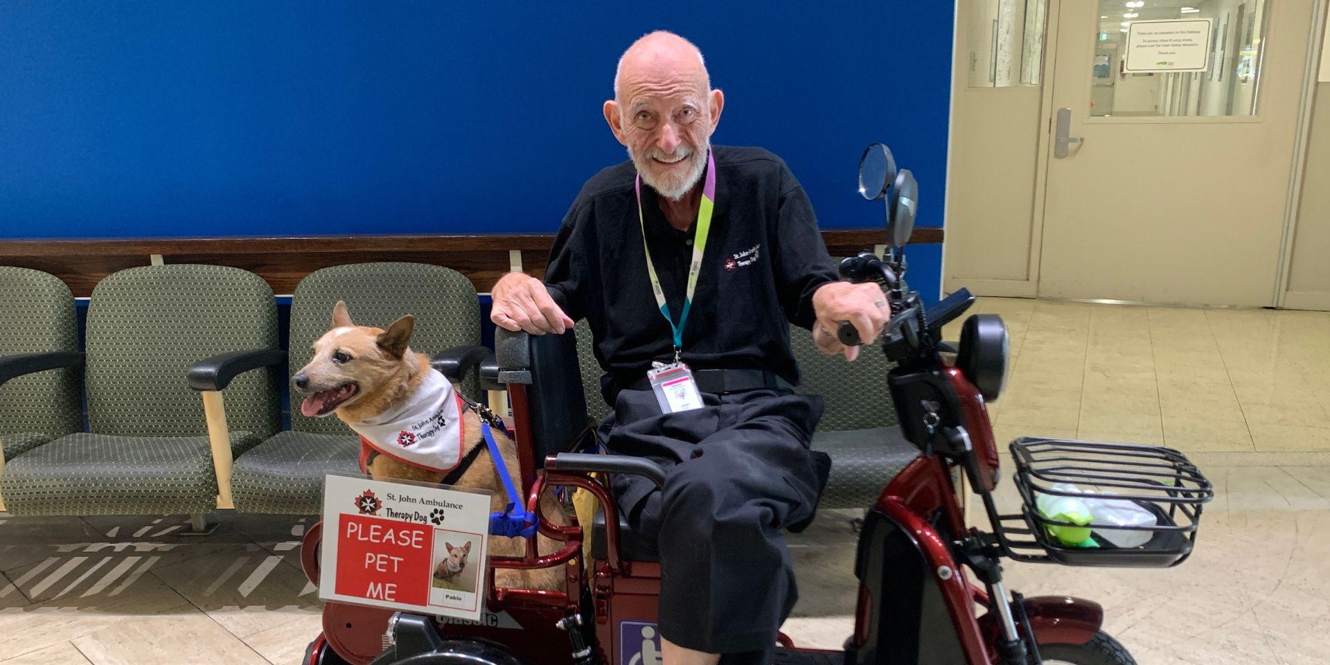 John Harper sitting on an electronic scooter with pet therapy dog Pablo