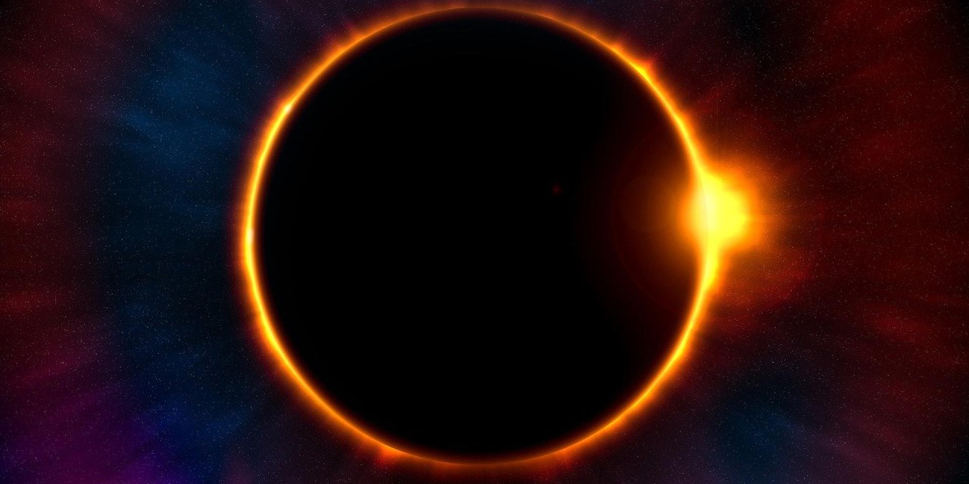 An image of a solar eclipse. The moon is covering the sun in a starry sky with only the edges of the sun visible. 