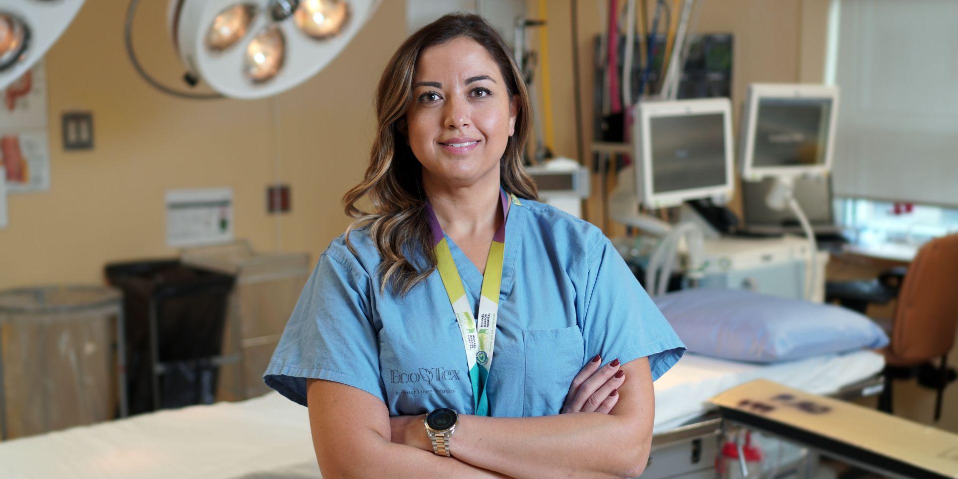 A doctor smiling and standing with her arms crossed in an operating room.