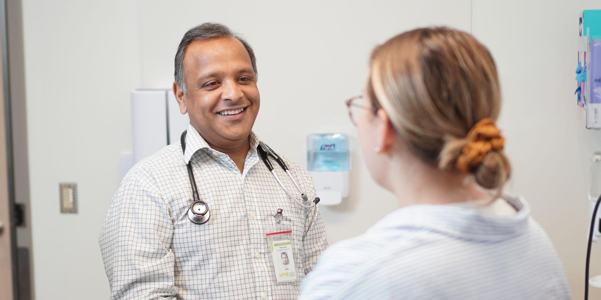 A doctor stands, smiling at a patient who is sitting down.