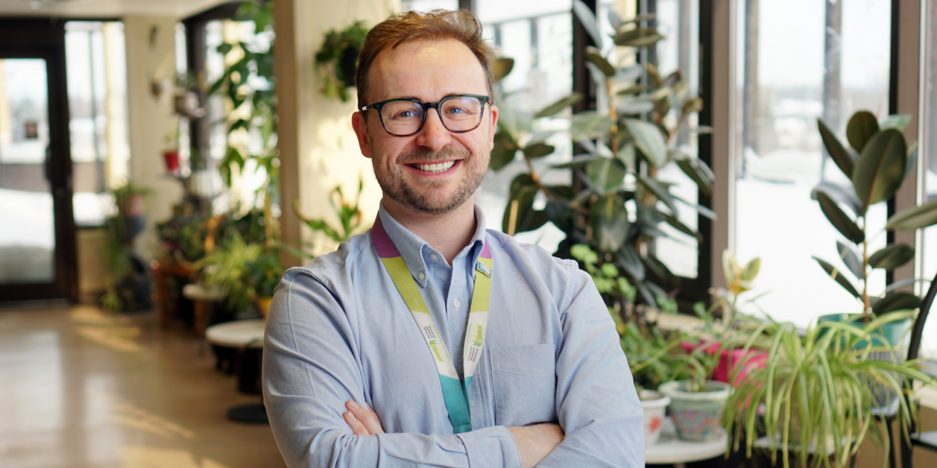 Man stands with arms crossed in room with plants. 