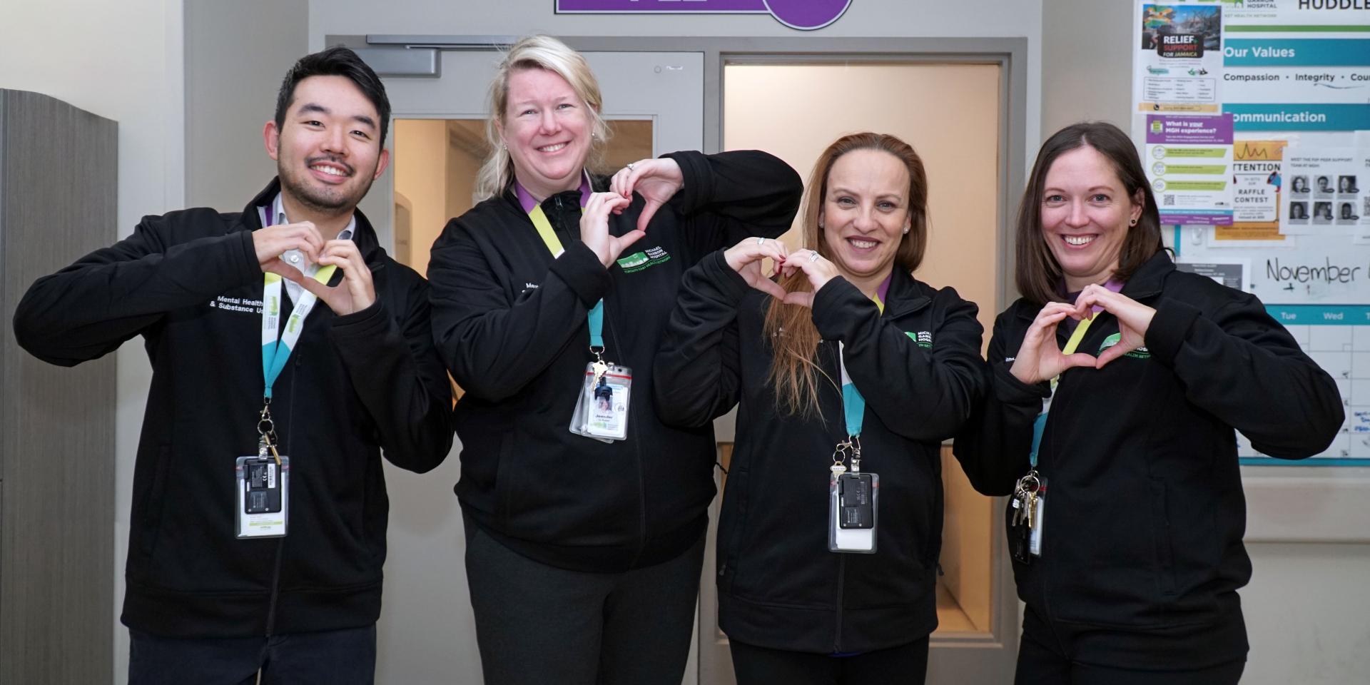 Four staff with badges are making hearts with their hands and smiling at the camera