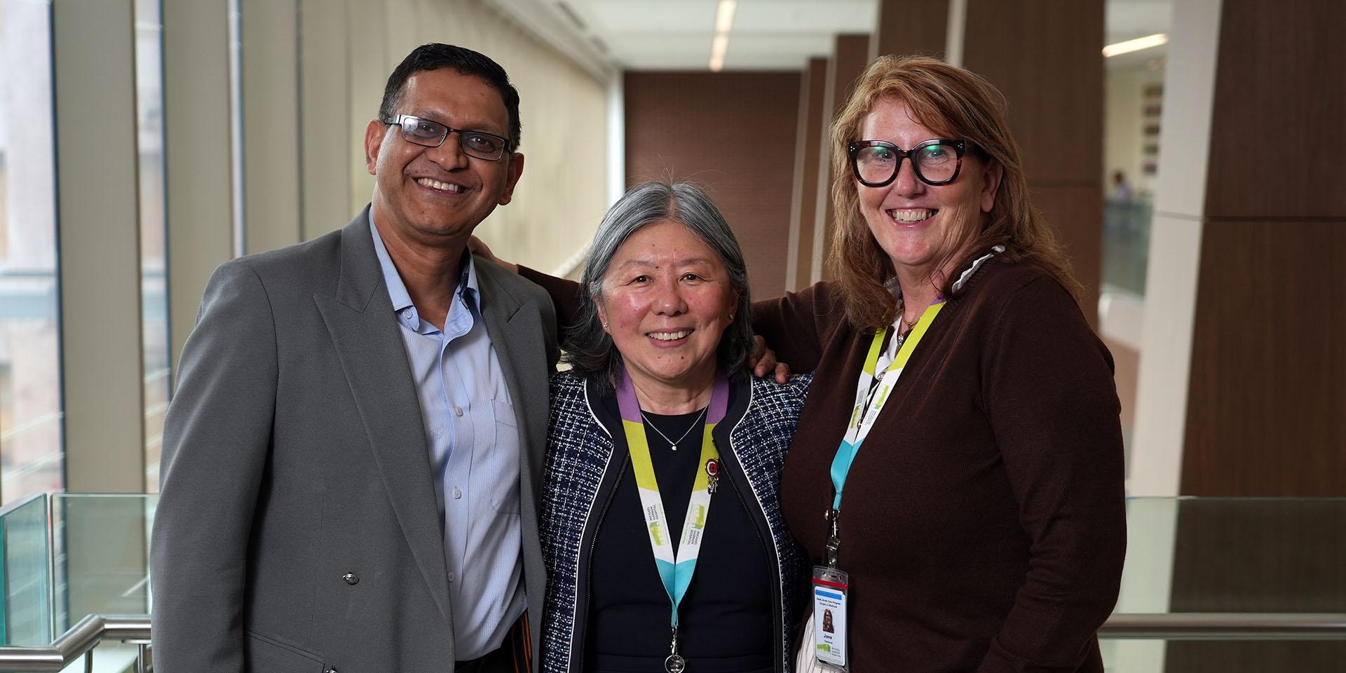 One man and two women stand smiling at the camera in a hospital hallway.