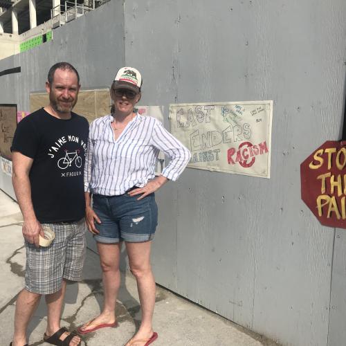 Members of the community standing beside messaging on construction fencing