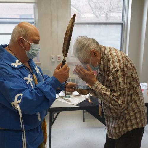 Elder Little Brown Bear smudges Red Eagle during his COVID-19 vaccine appointment at the clinic.
