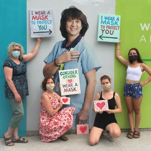 Four people wearing masks posing with a photo of a nurse 
