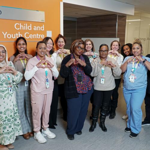 A group of Michael Garron Hospital staff posting outside of BMO Child and Youth Centre making hearts with their hands.