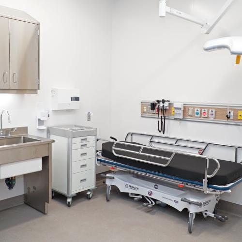 A hospital clinic room with a stretcher, desk and office chair.