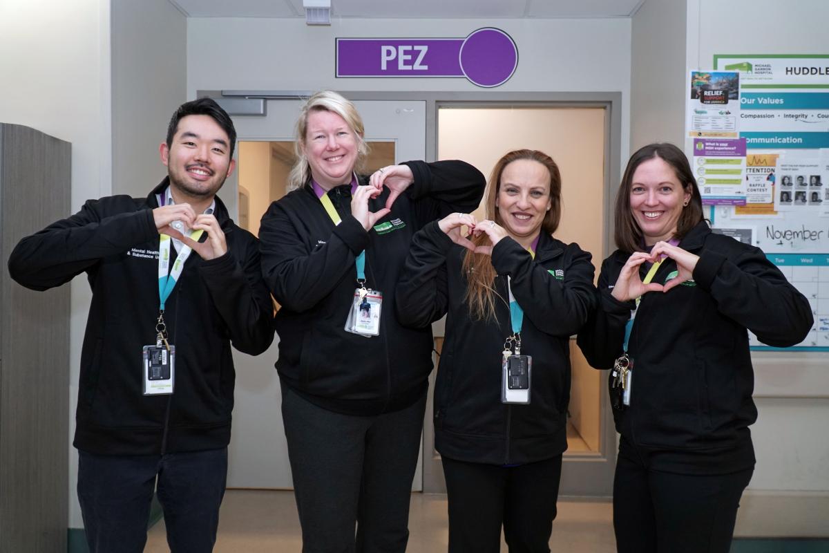Four staff with badges are making hearts with their hands and smiling at the camera