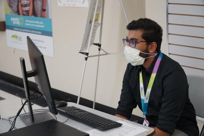 Screener Piranavvan Nagarajan wears a mask in front of a computer