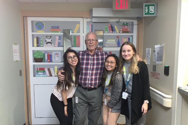 Harm Hutt and occupational therapy students posing in front of mural in memory care unit