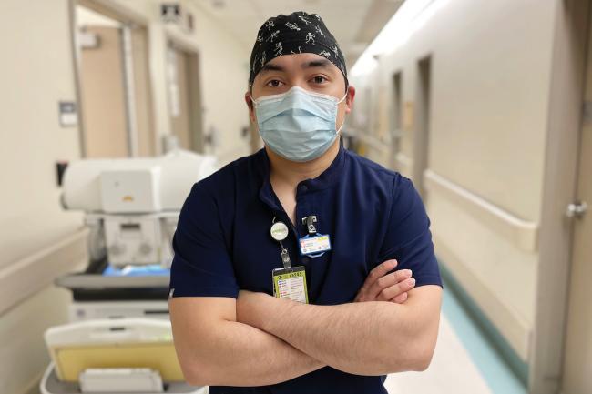 A hospital worker stands in a hallway looking at the camera