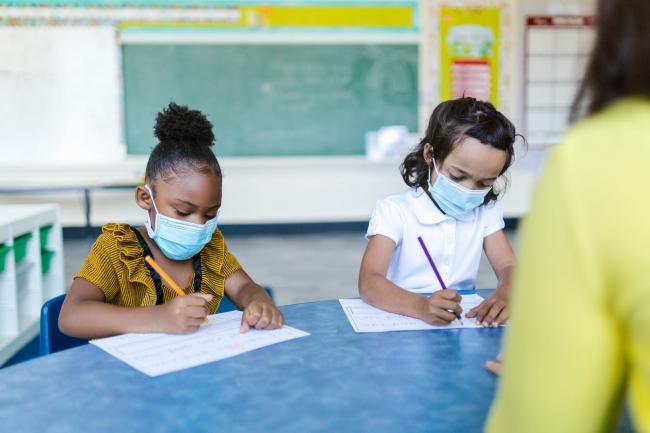 Two children sit at a desk at school.