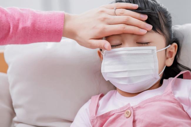 Hand on a childs forehead checking their temperature.