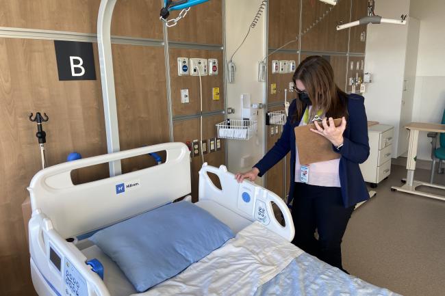 Carolyn Hay, Project Manager of the Redevelopment team at Michael Garron Hospital, stands on the left side of an inpatient bed in the new Thomson Centre