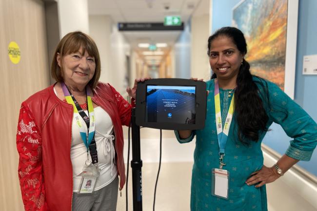 Two MGH staff members stand beside an iPad on a wheeled stand displaying the Voyce app