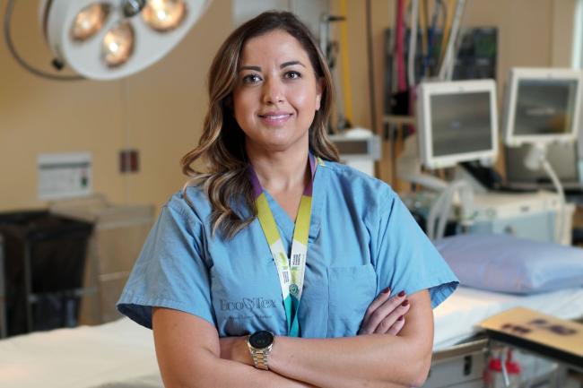 A doctor smiling and standing with her arms crossed in an operating room.