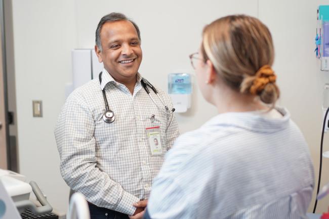 A doctor stands, smiling at a patient who is sitting down.