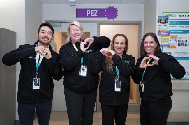 Four staff with badges are making hearts with their hands and smiling at the camera