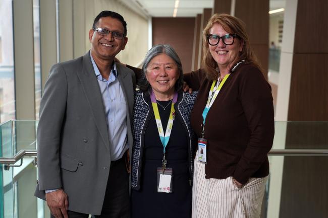 One man and two women stand smiling at the camera in a hospital hallway.