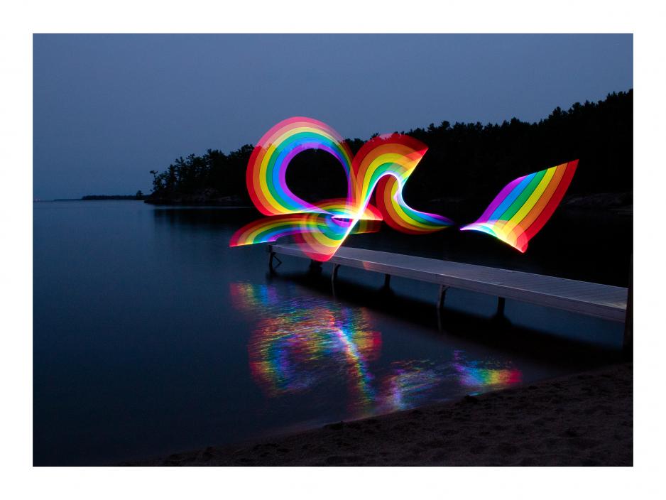 A curved rainbow floating above a dock and reflecting its image onto the water below it, artwork by Hugh Elliot