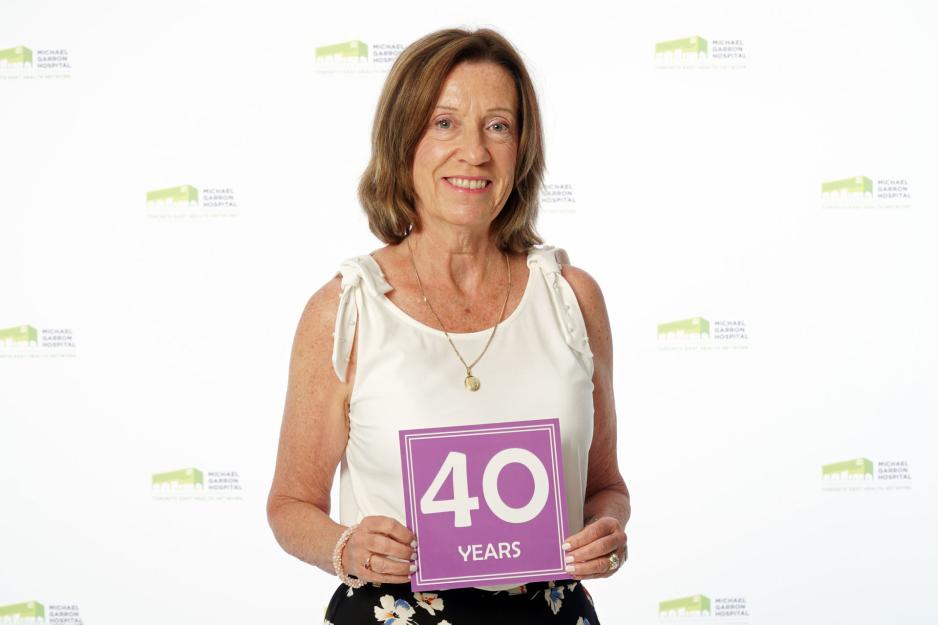 A staff member standing in front of a backdrop with the MGH logo and holding a sign that reads "40 years".