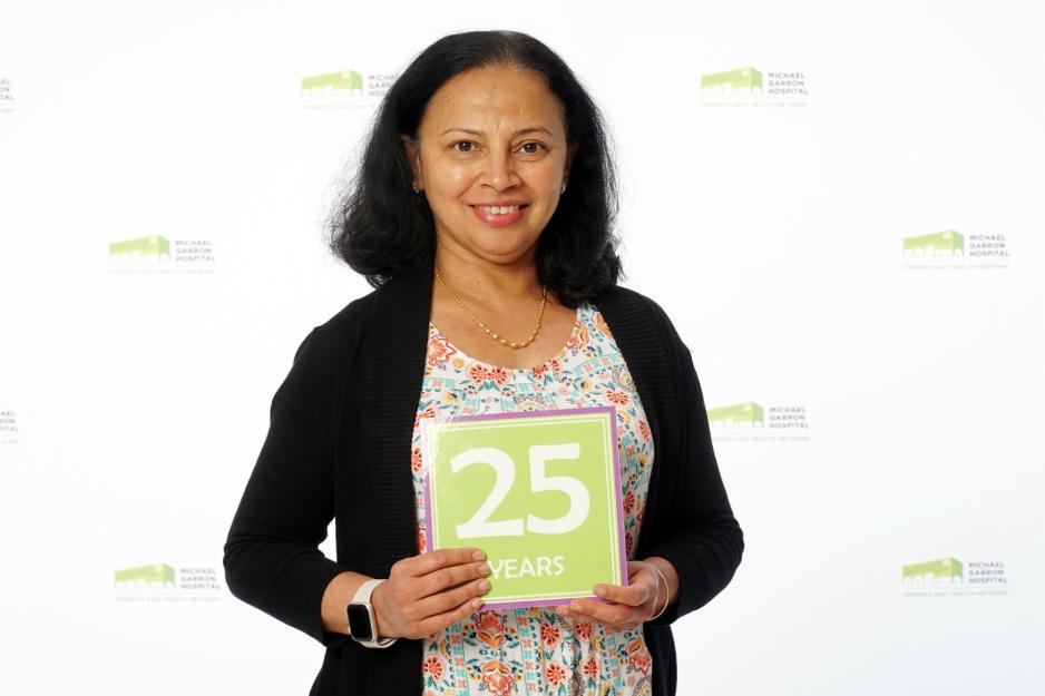 A staff member standing in front of a backdrop with the MGH logo and holding a sign that reads "25 years".
