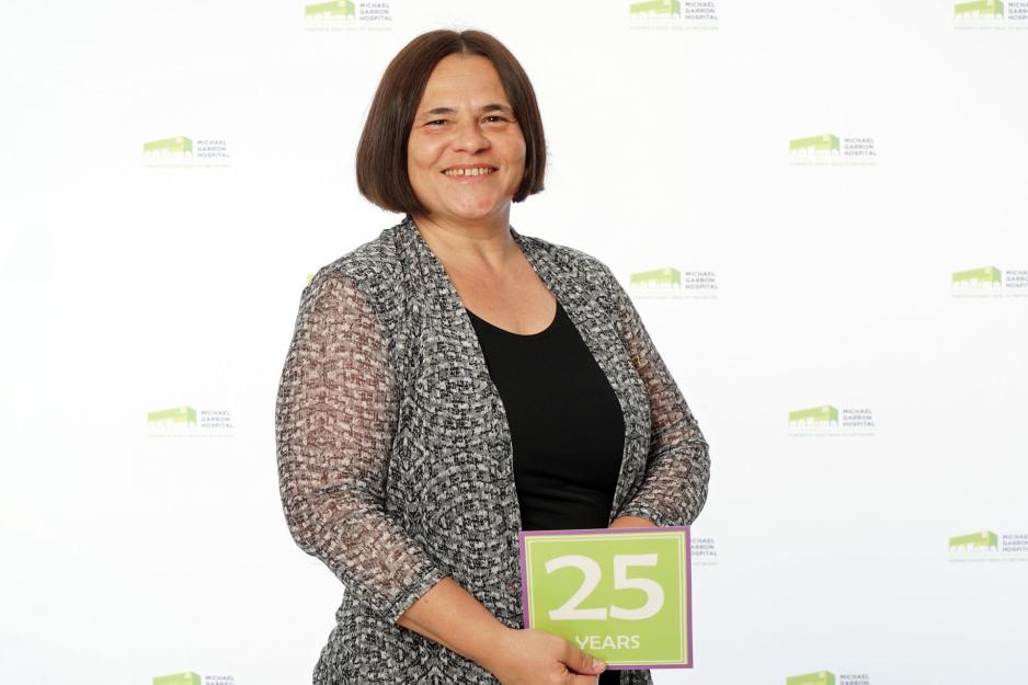 A staff member standing in front of a backdrop with the MGH logo and holding a sign that reads "25 years".