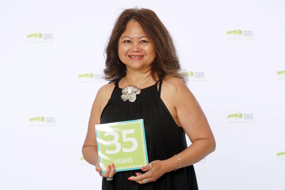A staff member standing in front of a backdrop with the MGH logo and holding a sign that reads "35 years".