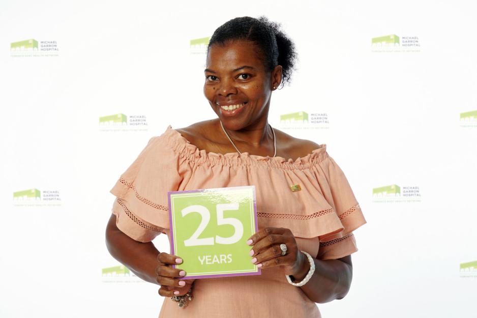 A staff member standing in front of a backdrop with the MGH logo and holding a sign that reads "25 years".