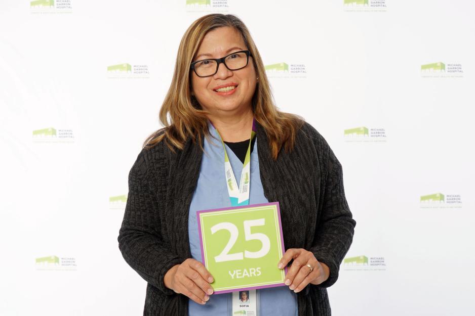 A staff member standing in front of a backdrop with the MGH logo and holding a sign that reads "25 years".