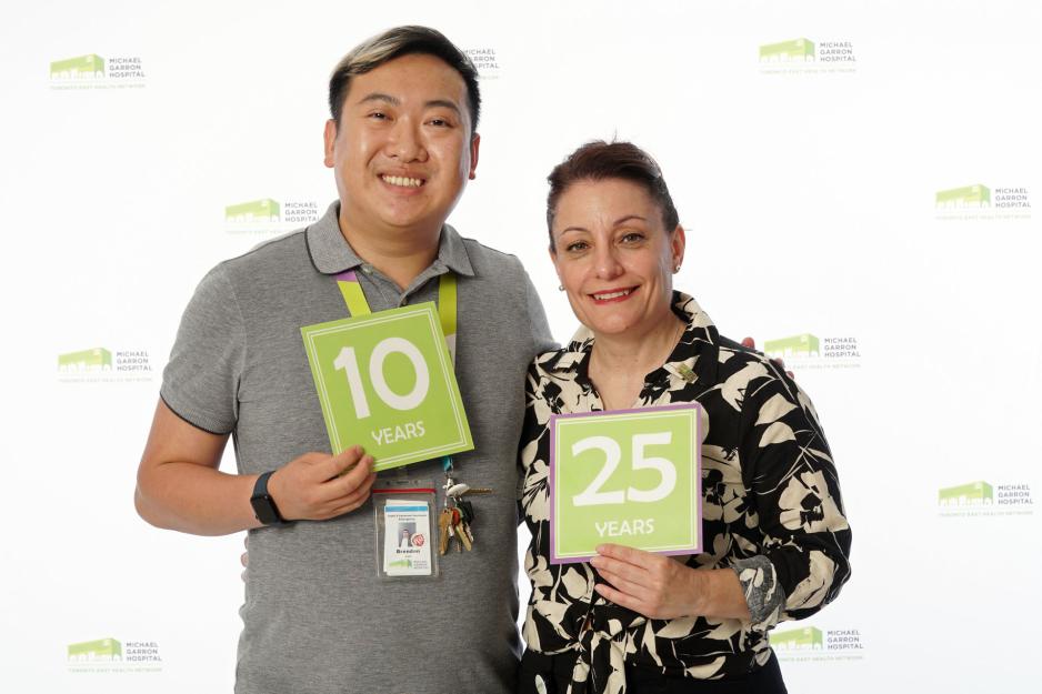 A staff member standing in front of a backdrop with the MGH logo and holding a sign that reads "25 years".
