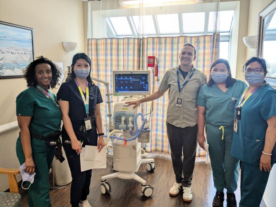 Healthcare workers standing beside a new mechanical ventilator.