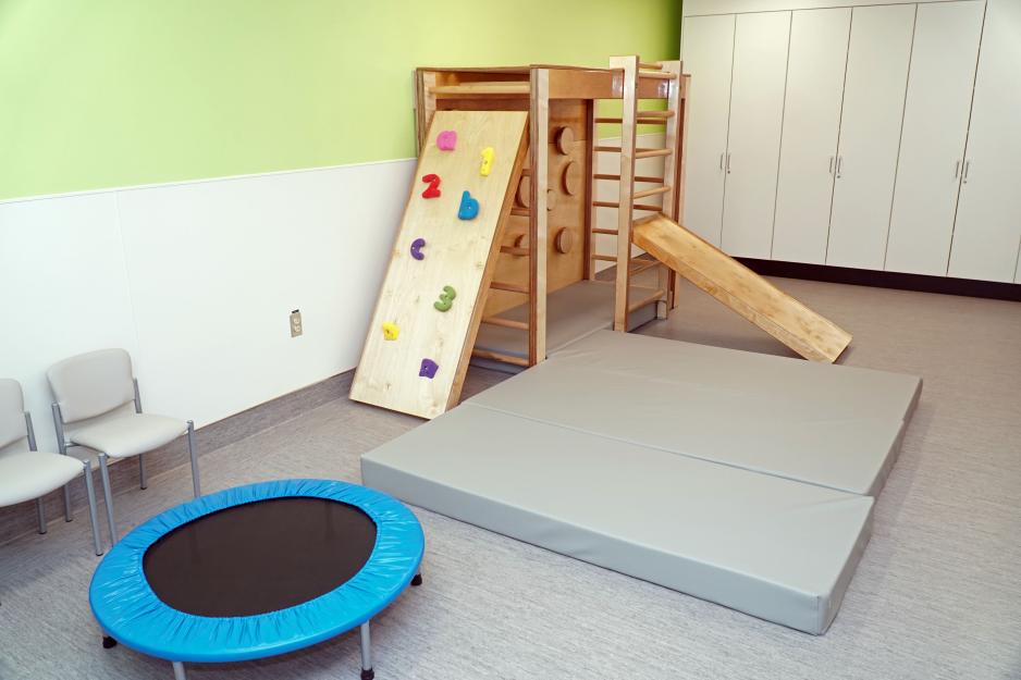 A room with a climbing structure, mat and trampoline.