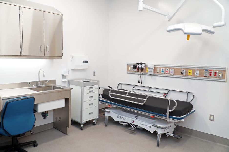 A hospital clinic room with a stretcher, desk and office chair.