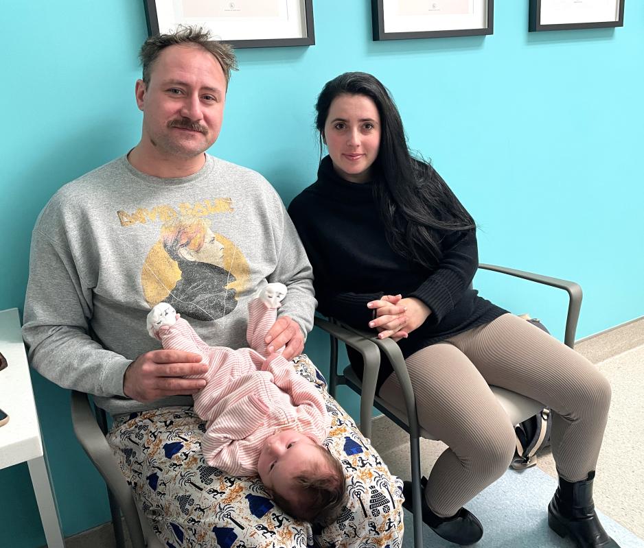 Two parents pose sitting with their infant on their lap at a clinic.