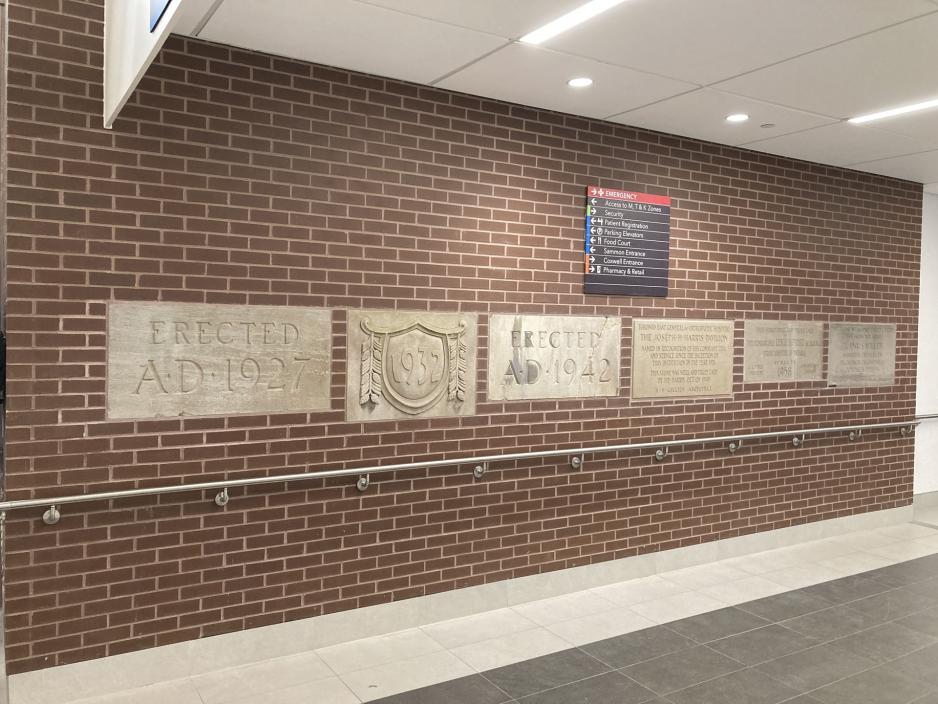 Four historic limestone cornerstones mounted on a red brick wall displaying carved text in hospital corridor.