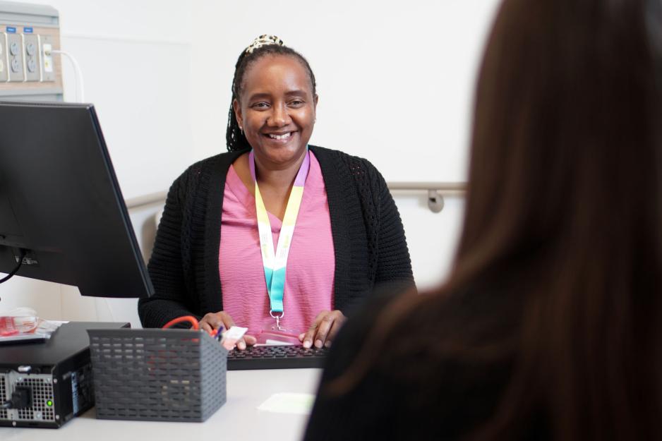 A staff member sits at a computer and talks to a patient.